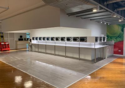 A row of microwaves is displayed on a counter in a brightly lit, modern showroom with wood and tile flooring.
