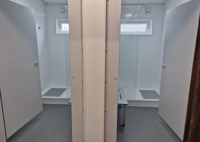 Two shower cubicles with frosted glass doors and grey floors separated by a partition in a clean, modern, and well-lit toilet facility.