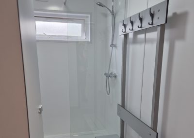 Modern shower with glass door, wall-mounted showerhead, window above, and metal coat rack with hooks on the right wall.